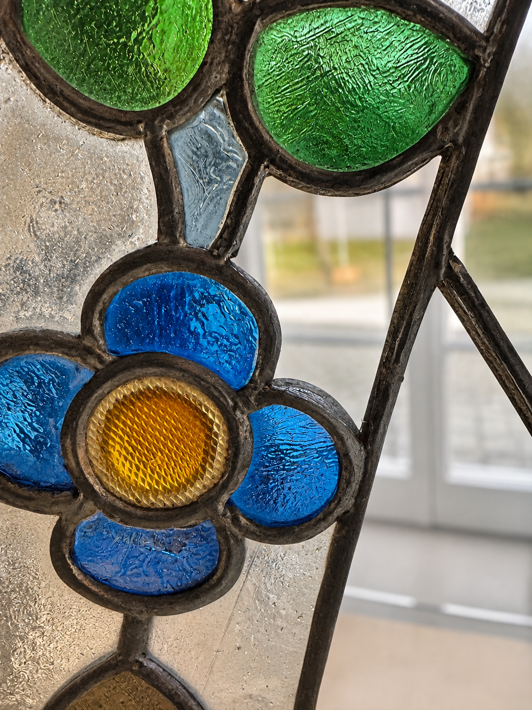 Detail einer Bleiverglasung mit blauer Blume, gelber Mitte und grünen Gläsern