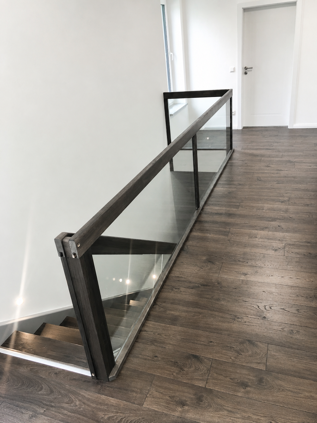 Glasgeländer an Galerie im Innenbereich mit dunklem Rahmen und Holzfußboden